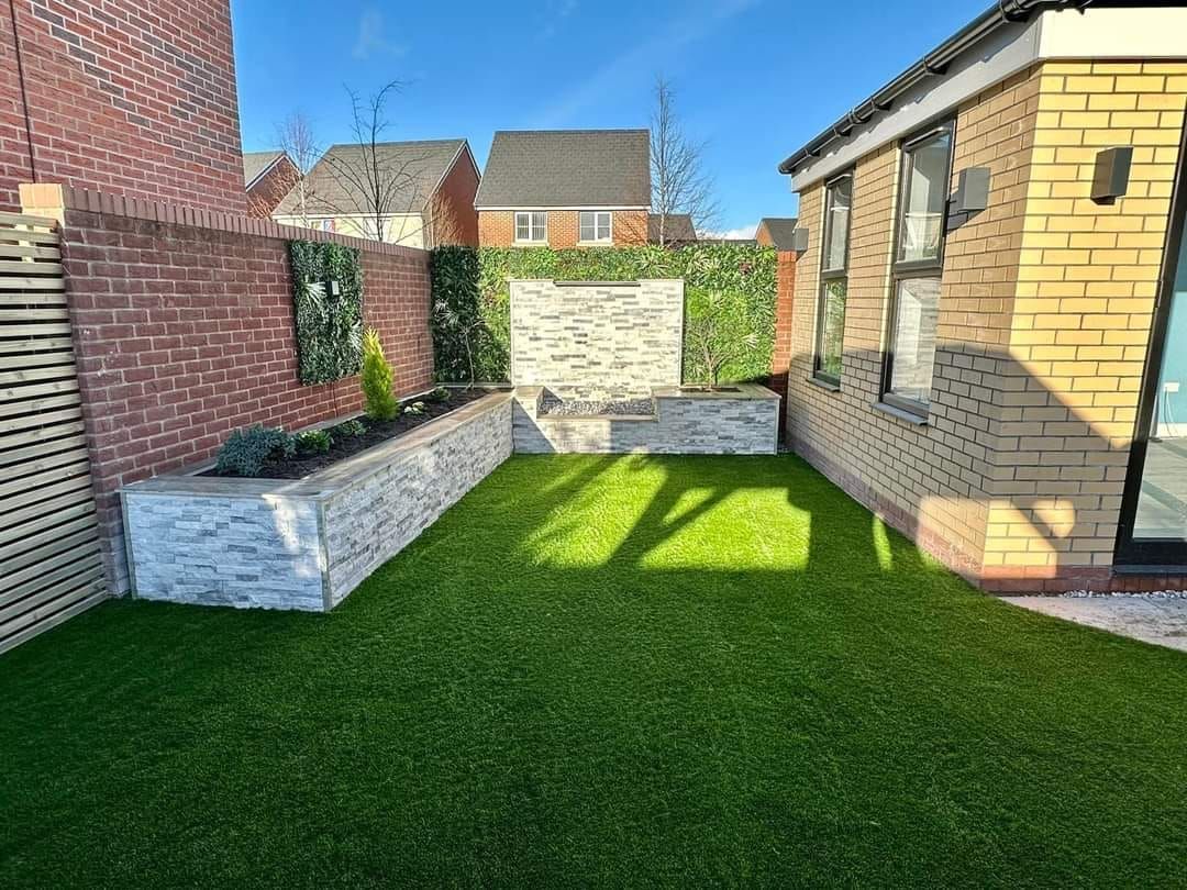 Small modern backyard with faux grass, brick walls, and decorative stone planters.