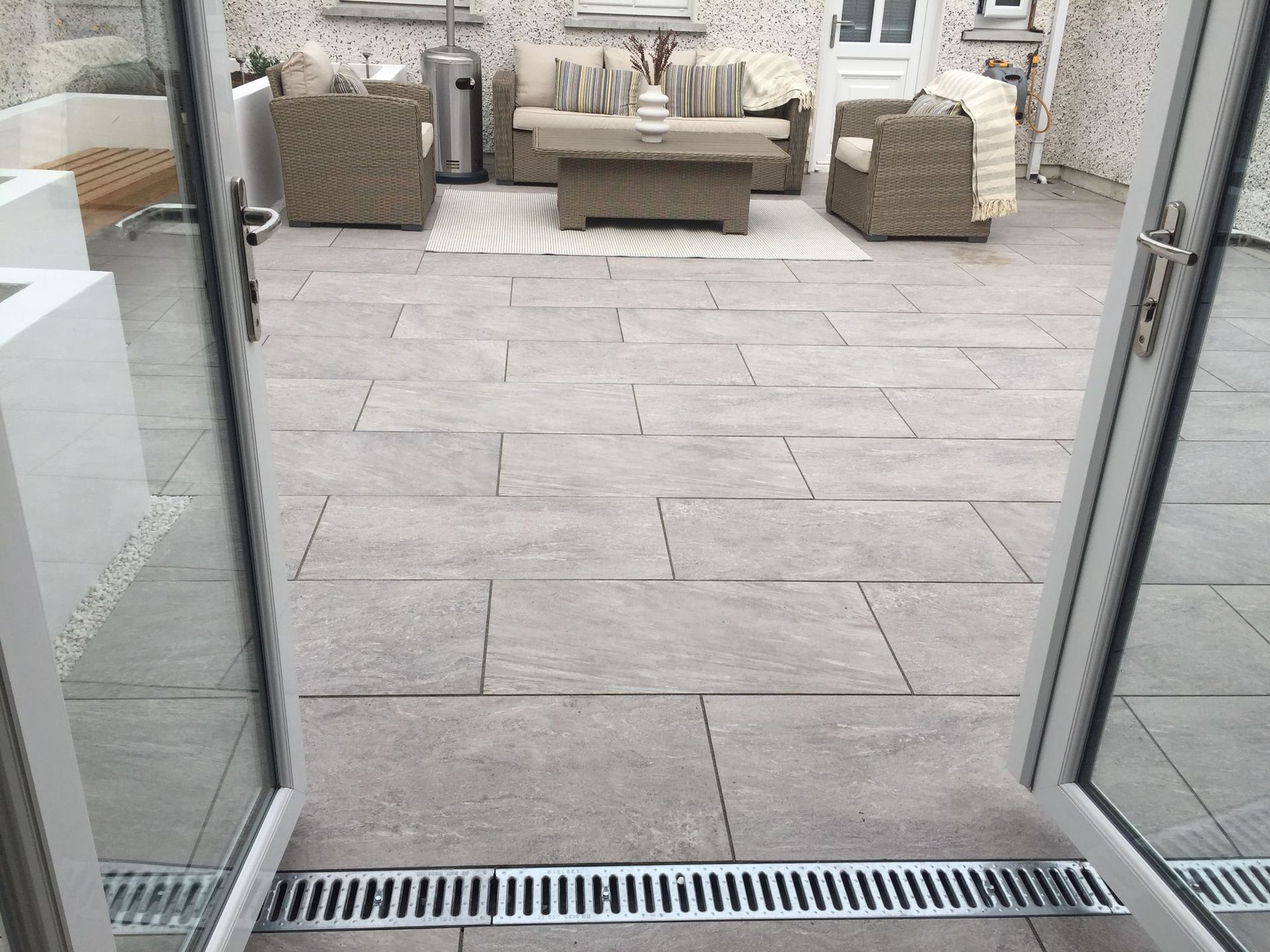 Open doors lead to a patio with stone flooring and outdoor furniture.