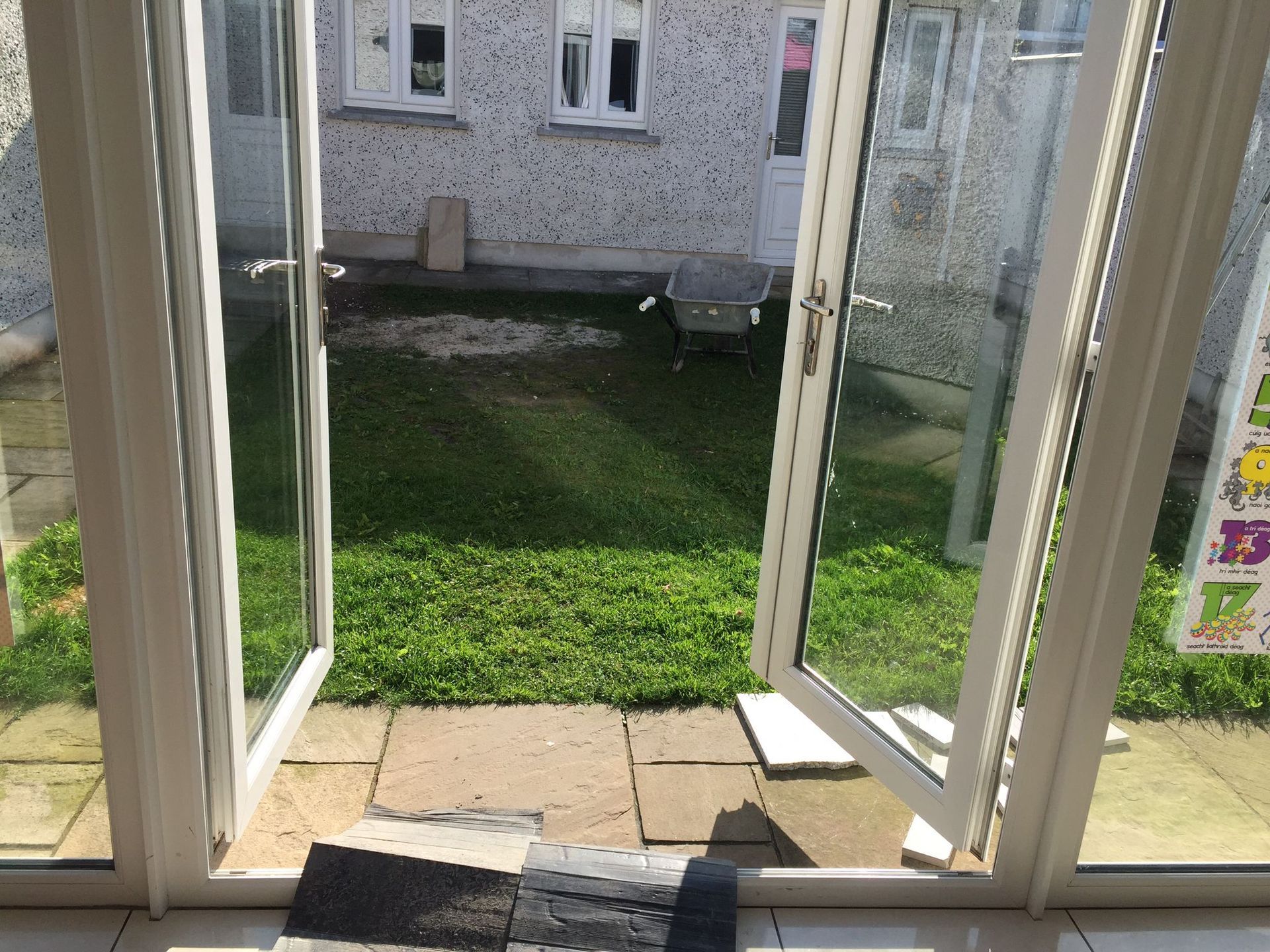 Open white-framed doors overlooking a green lawn and patio. Backyard with a building in the distance.