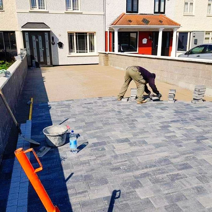 Man laying grey pavers on a driveway; house in the background.