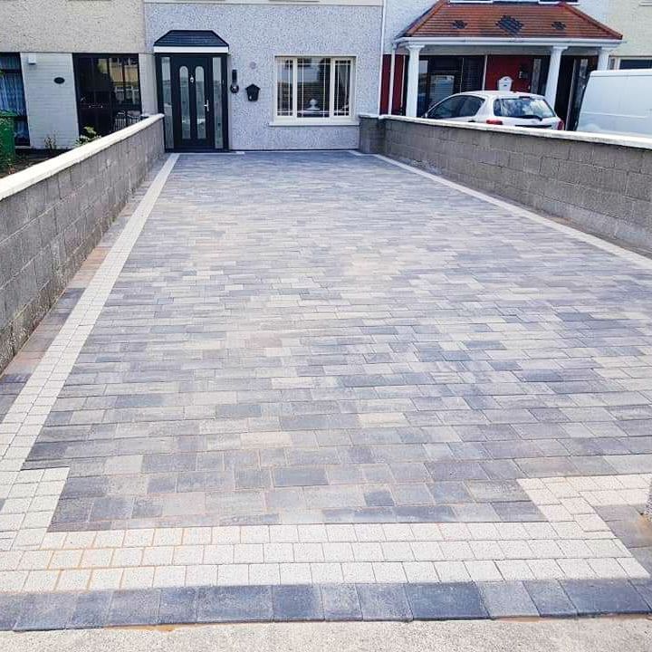 Driveway paved with gray bricks, bordered by light-colored bricks, leading to a house.