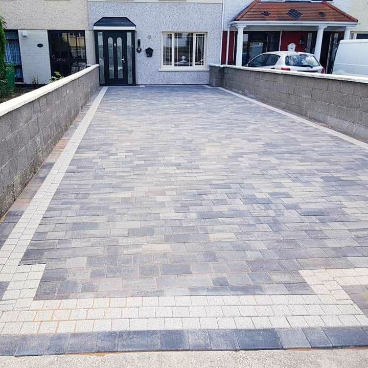 Driveway paved with grey blocks, bordered by light-colored blocks and walls, leading to a house.