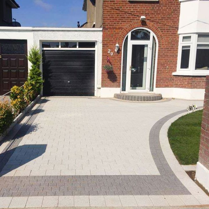 Driveway with light gray pavers, dark gray border, lawn, garage, and brick house with glass door.