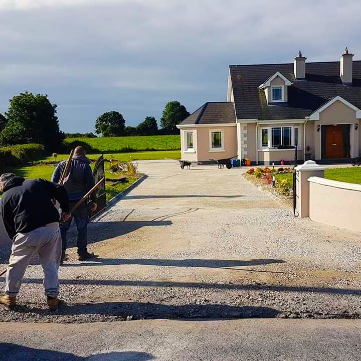 Men working on a gravel driveway in front of a house on a sunny day.