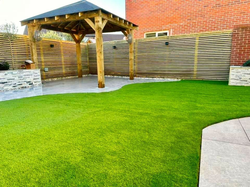 Green lawn with gazebo, wooden fence, brick wall.