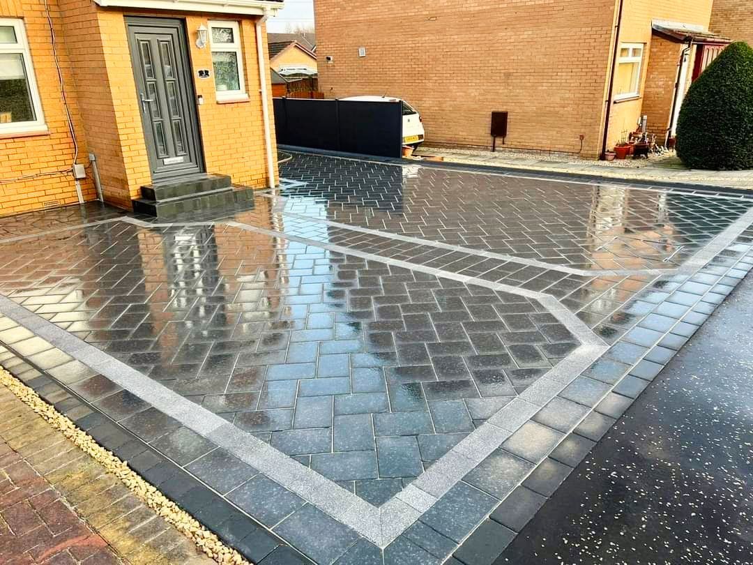 Paved driveway with dark gray blocks and light gray border, wet surface reflecting the sky.