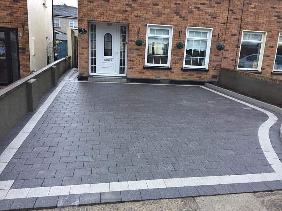 Brick driveway in front of a brick house with a white trim border.