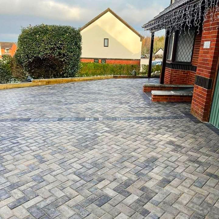 Brick paved driveway in a herringbone pattern, leading to a house with red brick and a green door.