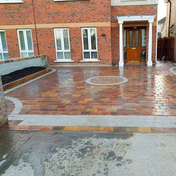 Brick driveway in front of a brick house with a brown door.