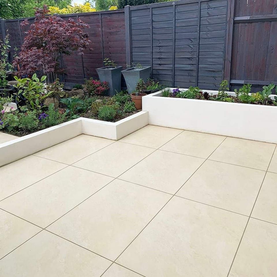 Beige patio with built-in planters filled with flowers, next to a garden and a wooden fence.
