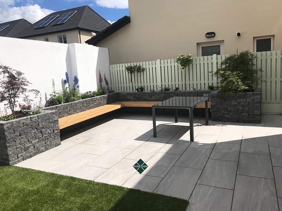 Patio with stone planters and a wooden bench, a table, and a light green fence.