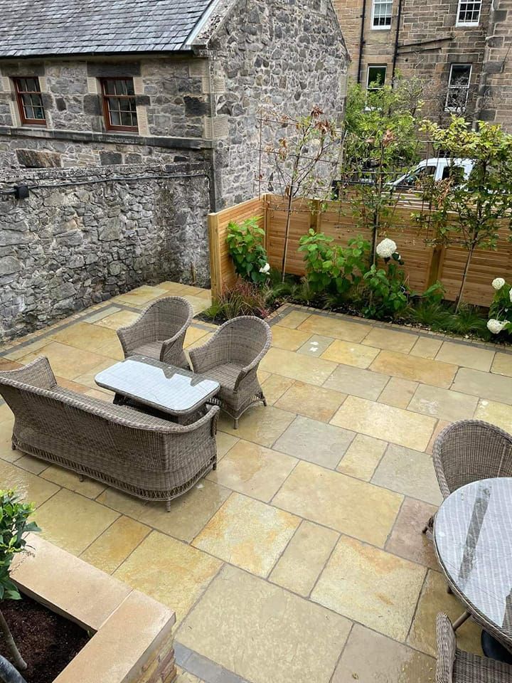 Patio with sandstone pavers, wicker furniture, stone wall, and garden area with wood fence.