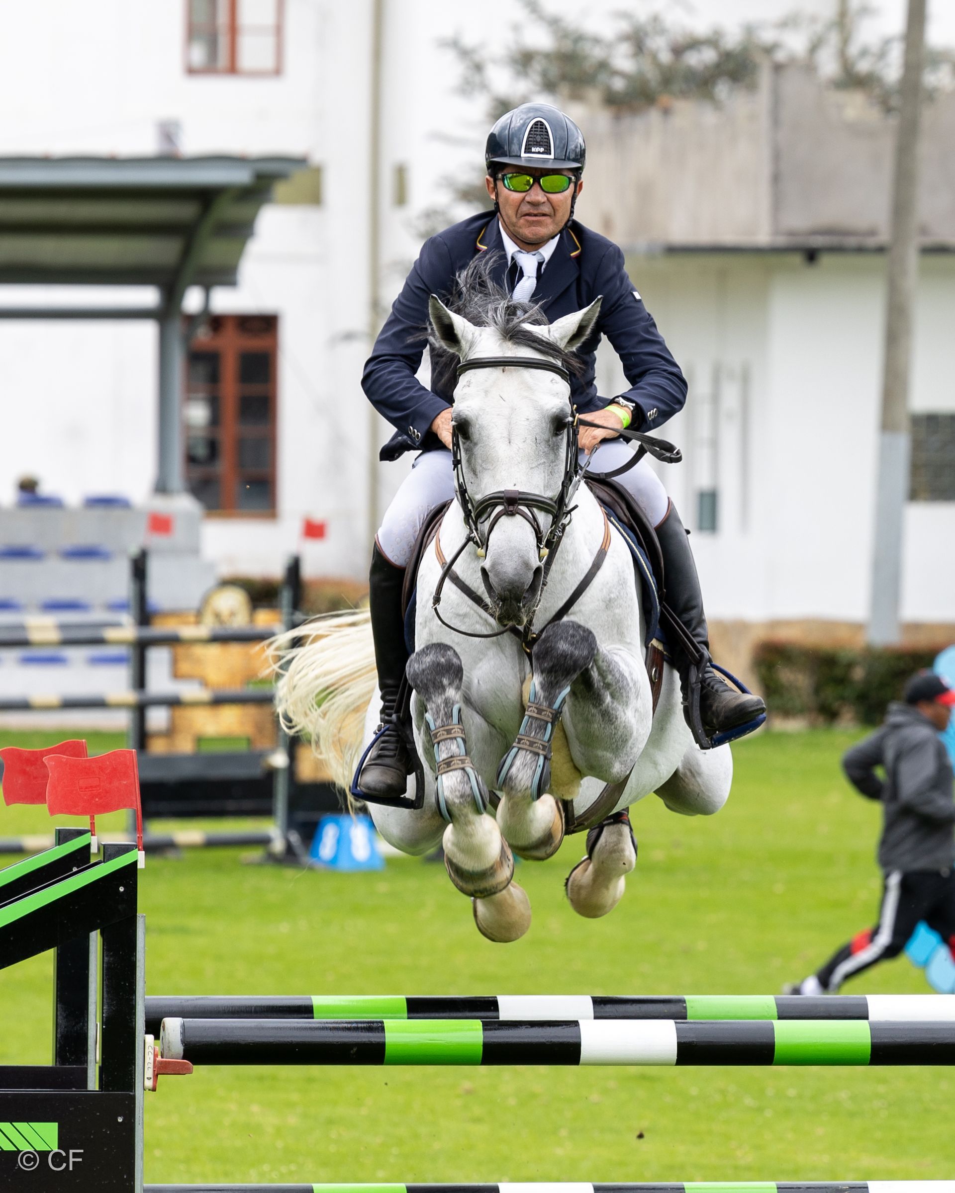 A man is riding a white horse over a hurdle.