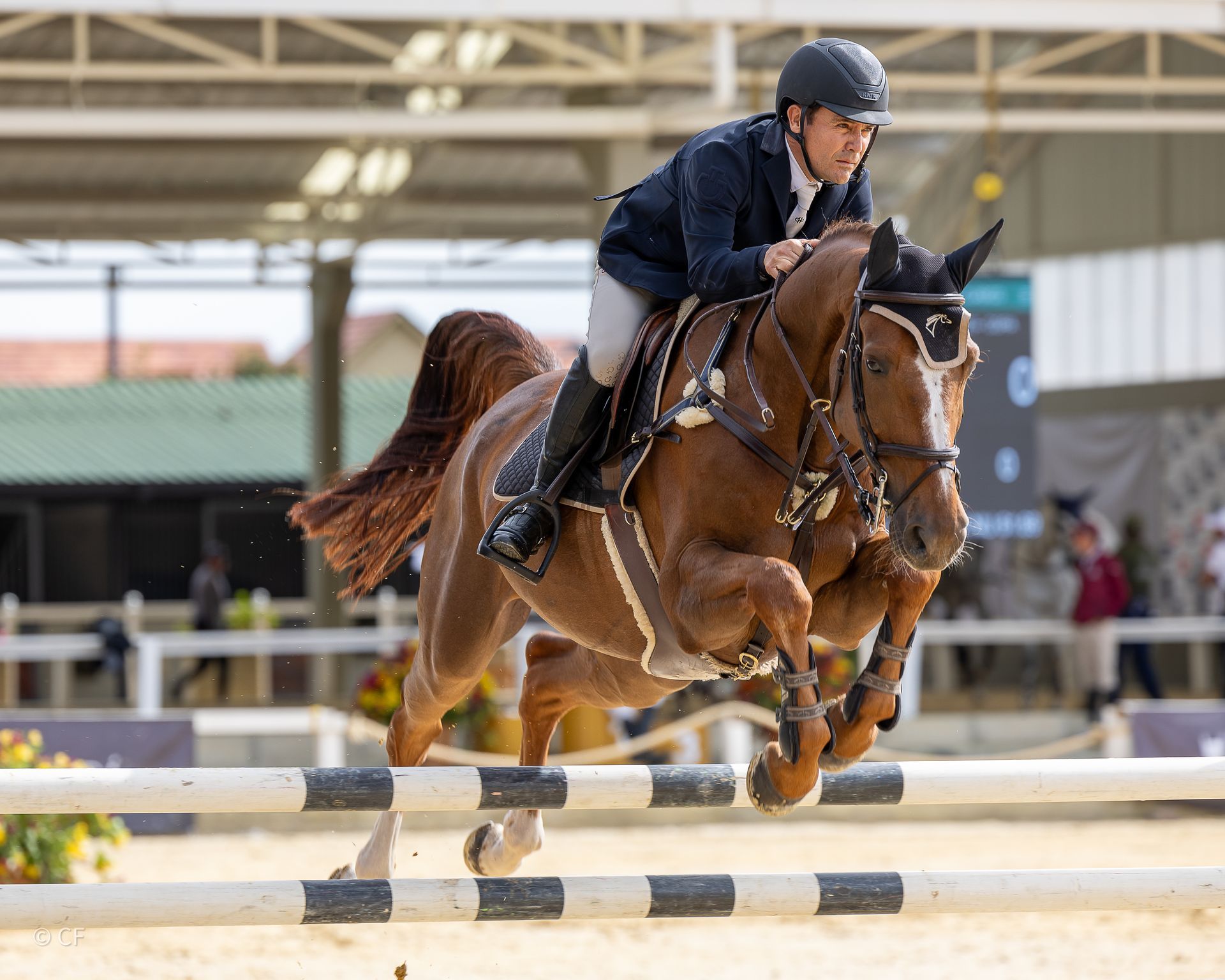 A man is riding a brown horse over a jump.