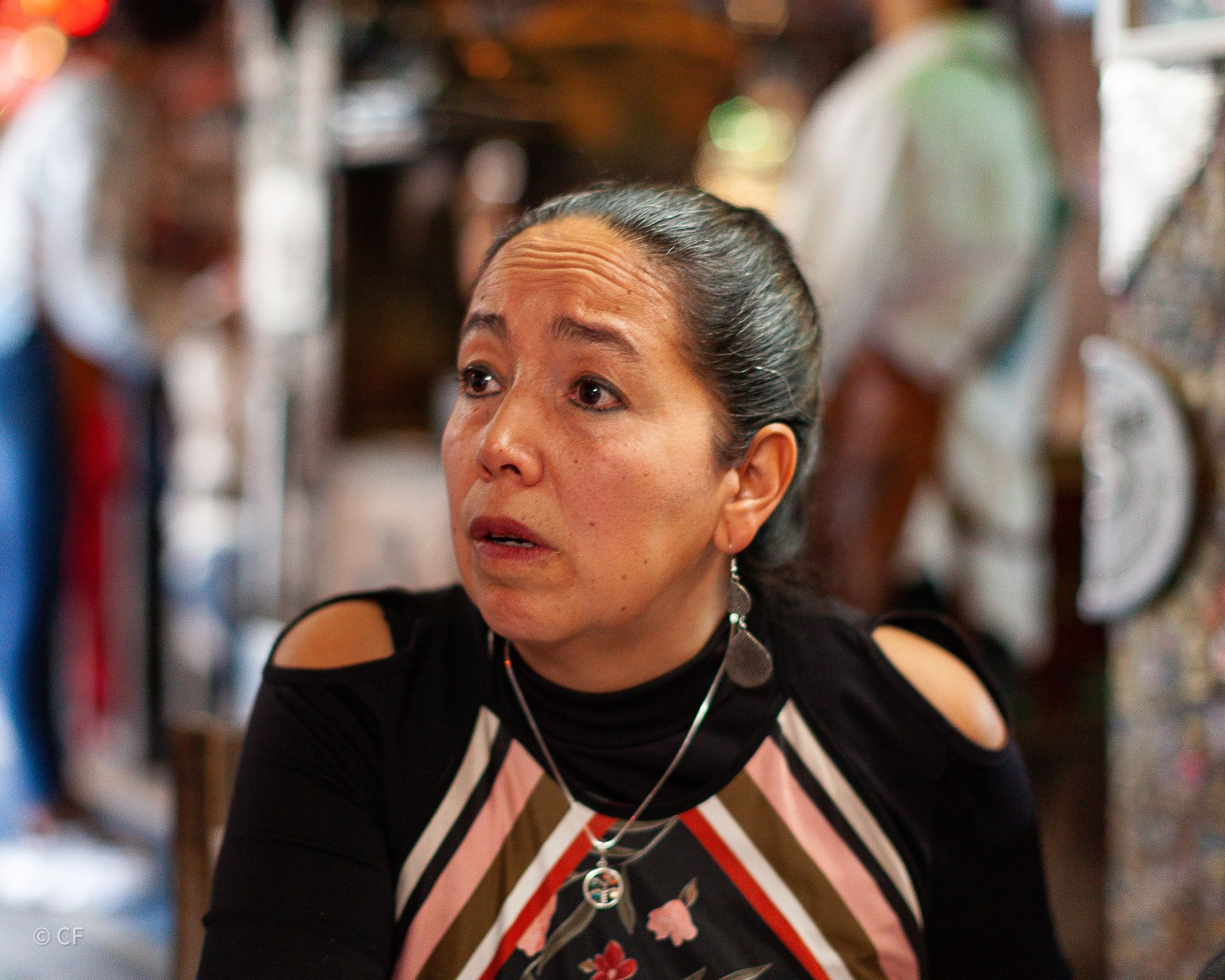 A woman wearing a striped dress and a necklace is sitting in a restaurant.