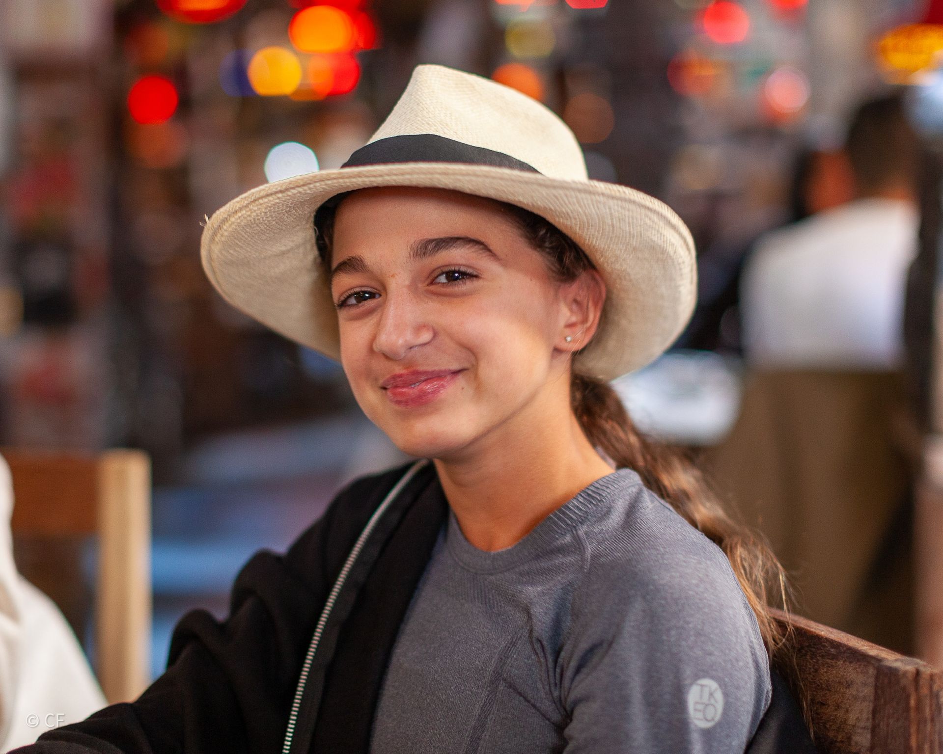 A young girl wearing a hat and a gray shirt is smiling for the camera.