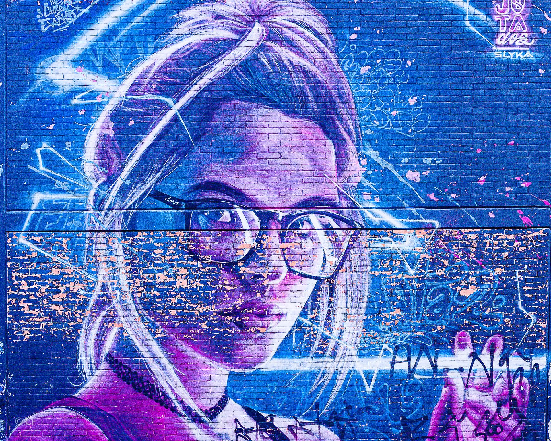 A painting of a woman wearing glasses on a brick wall.