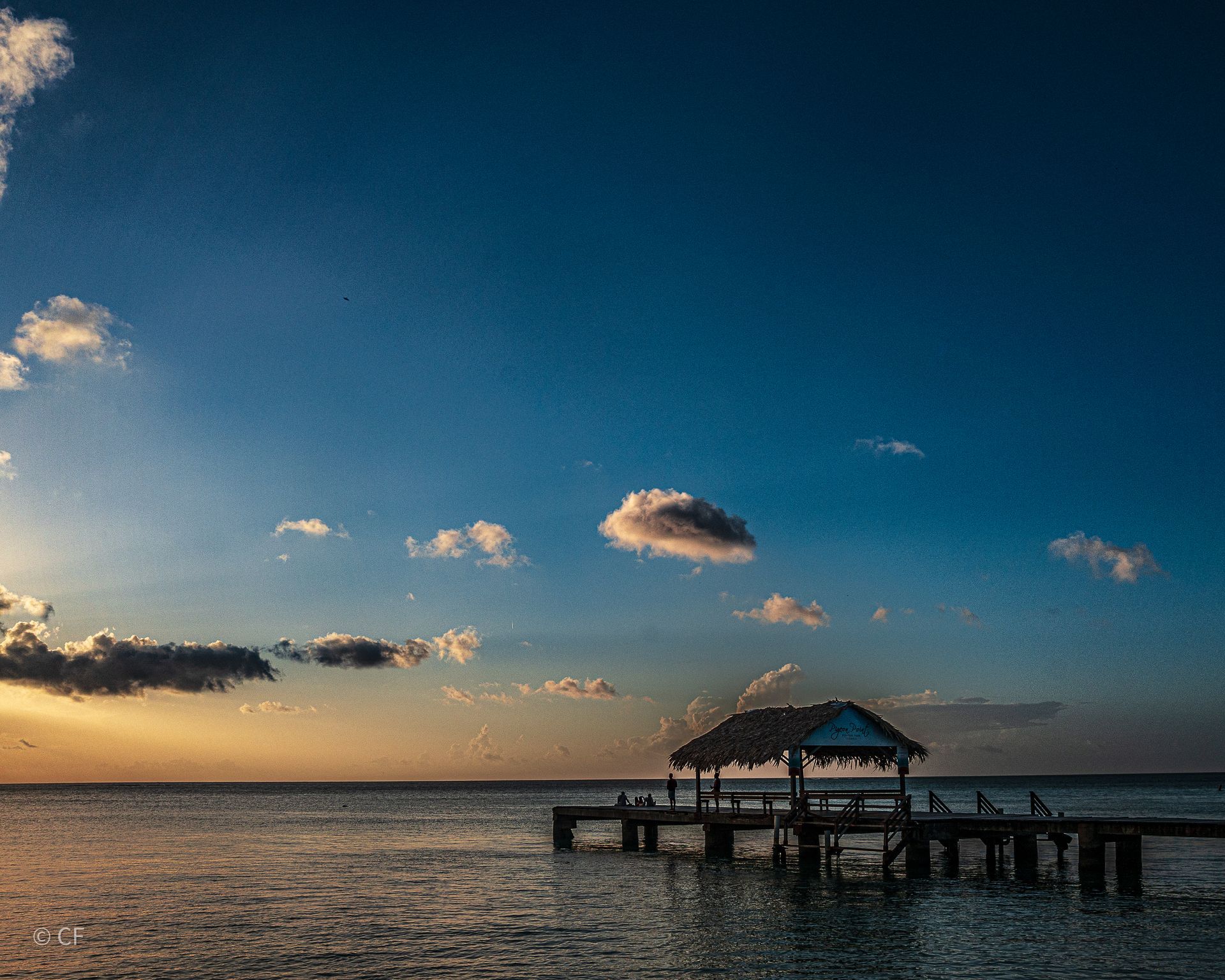 There is a dock in the middle of the ocean with a hut on it.