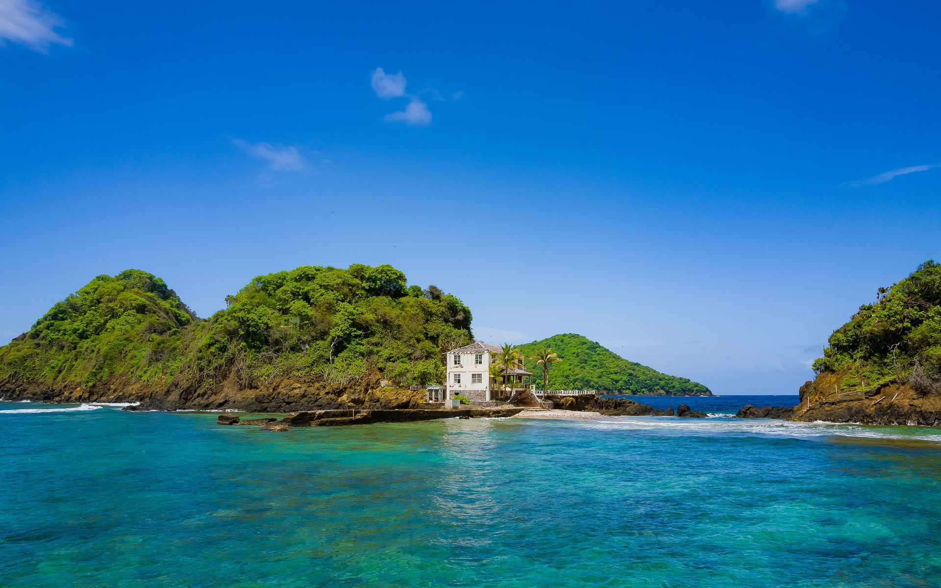 A small island in the middle of the ocean with a house on it.