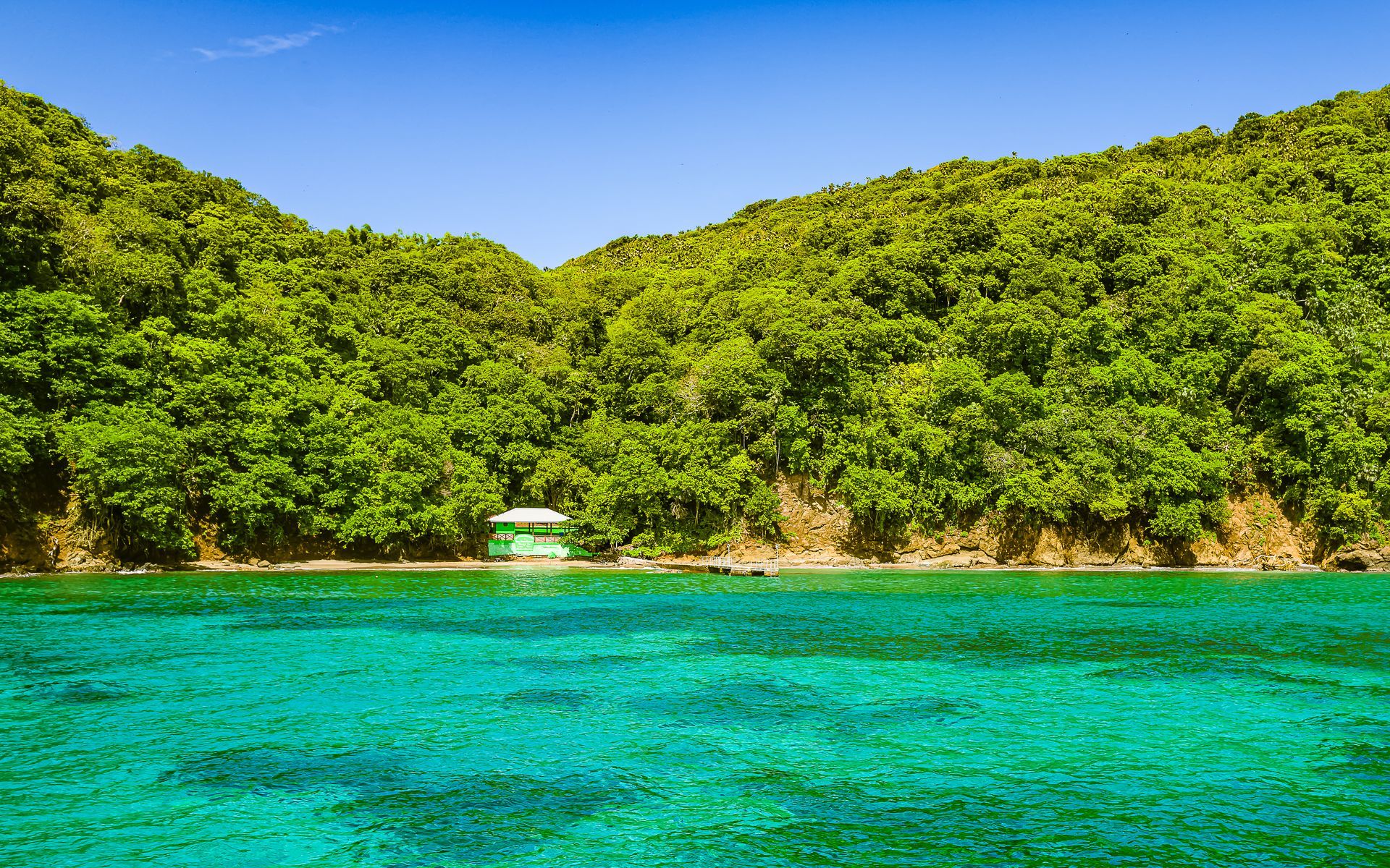 A boat is in the water near a lush green hillside.