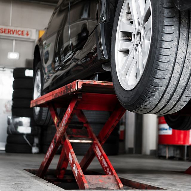 Black car raised on a red scissor lift in an auto repair shop, with a tire in the foreground