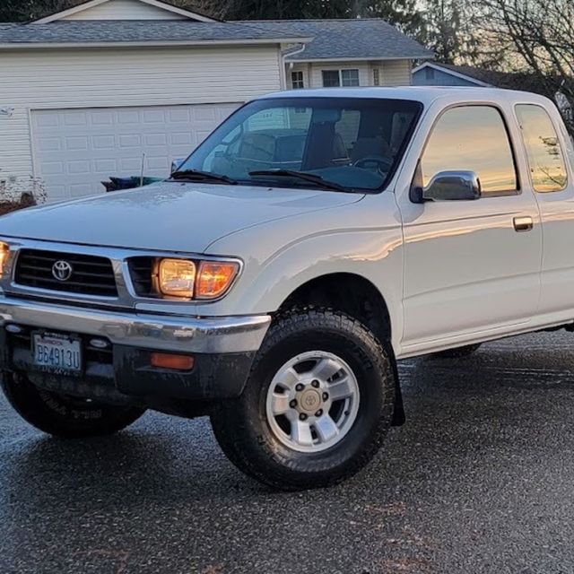 White Toyota pickup truck parked in a driveway at dusk, with headlights on in front of a garage.