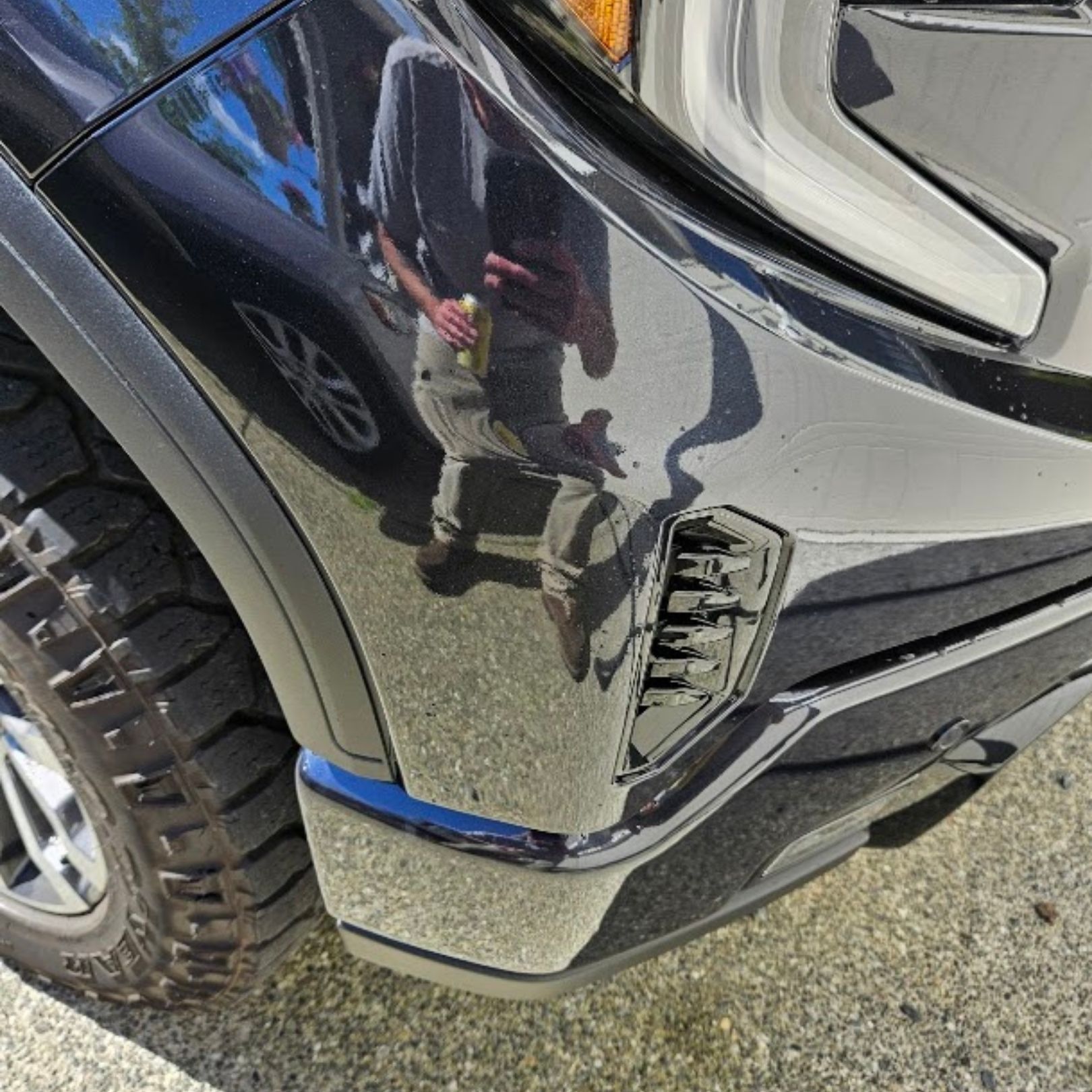 Close-up of a black car’s front bumper with a scuffed, damaged corner near the wheel.