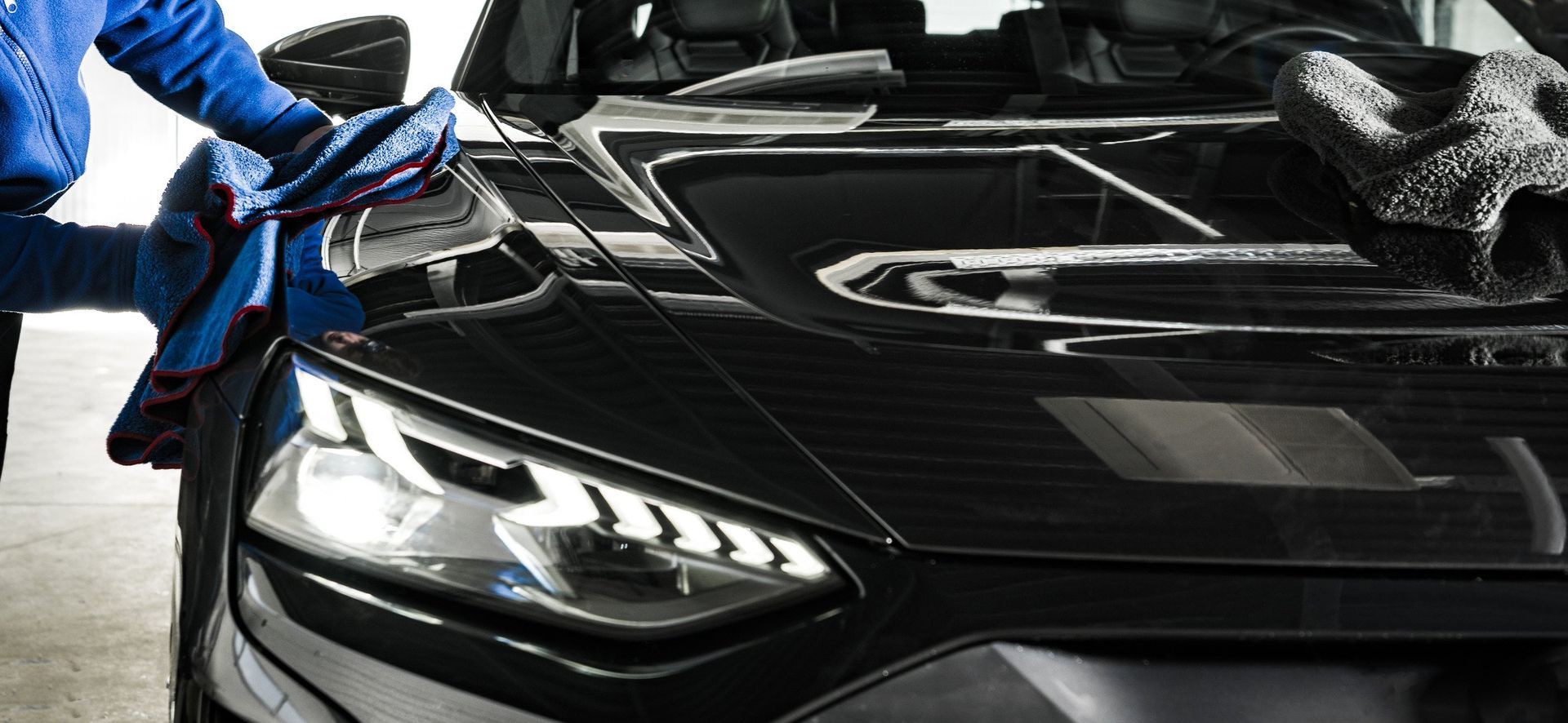 A man is cleaning the hood of a black car with a cloth.