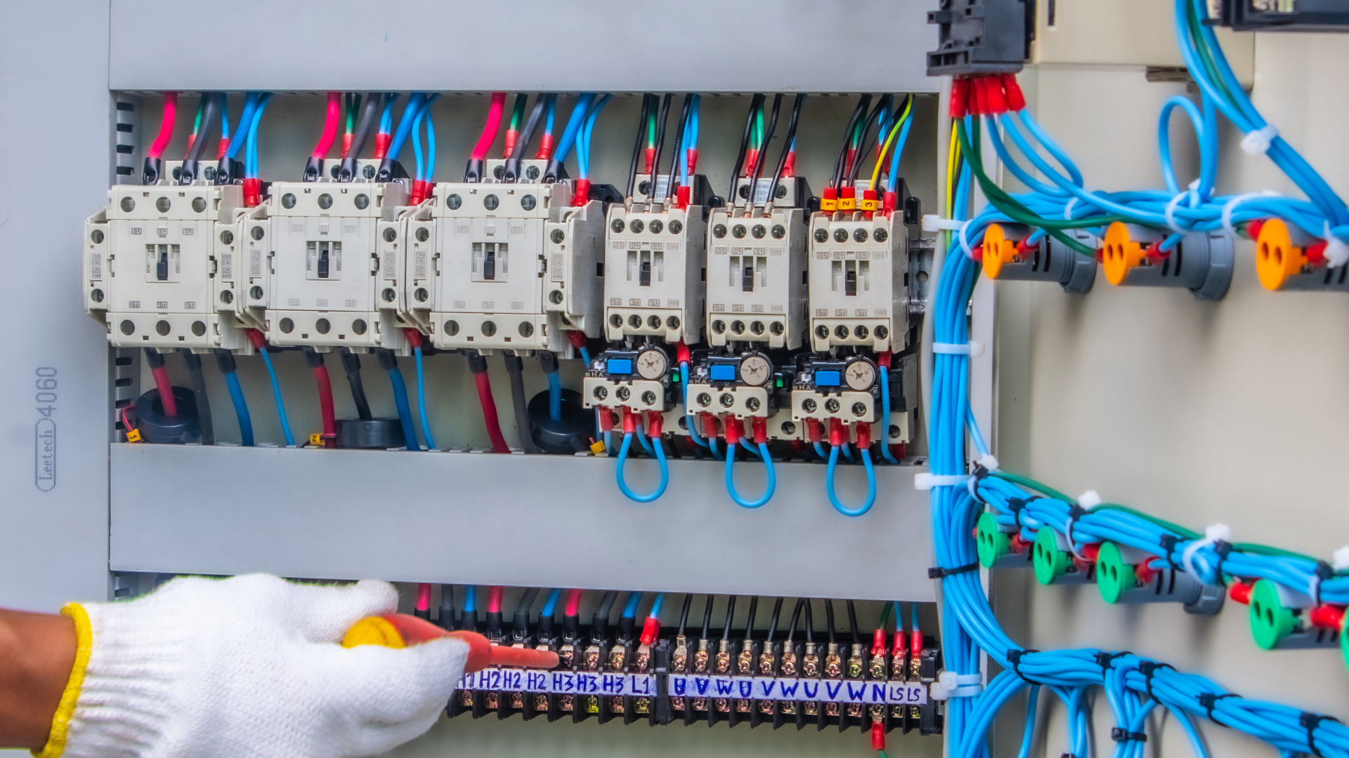 Electrician wiring a circuit breaker panel with blue cables in a control box