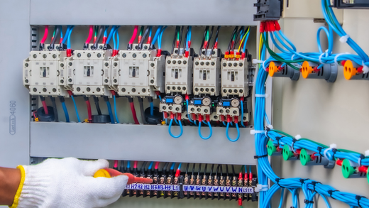 Electrician wiring a circuit breaker panel with blue cables in a control box