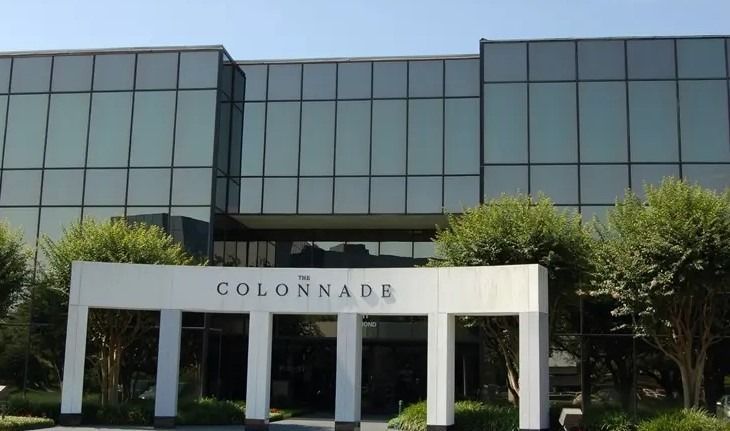 Modern office building with a white “COLONNABE” entrance sign and trees in front