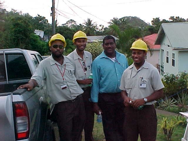 Four workers in yellow hard hats stand beside a pickup truck on a roadside.