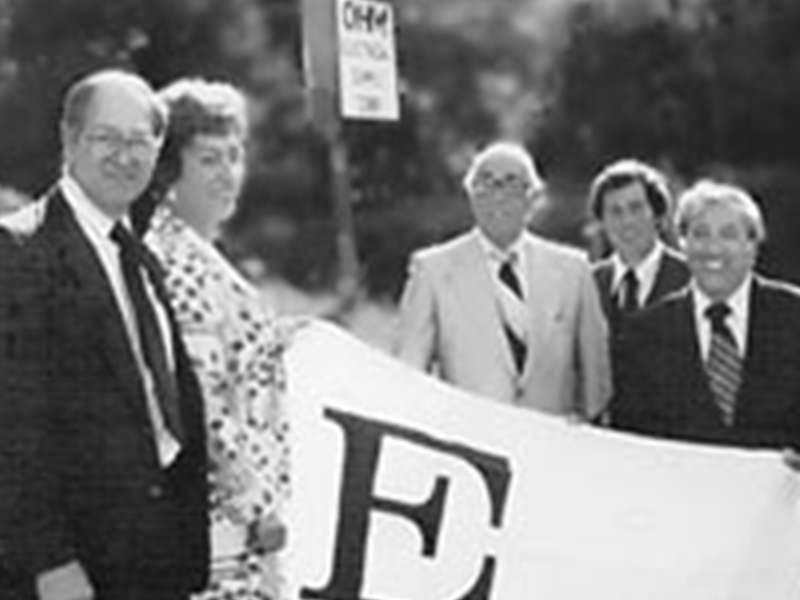 People standing outdoors holding a large banner with a big letter