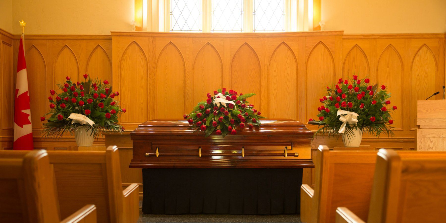 Funeral service chapel with wooden casket and red rose arrangements, highlighting Funeral Home and Cremations in Leominster, MA