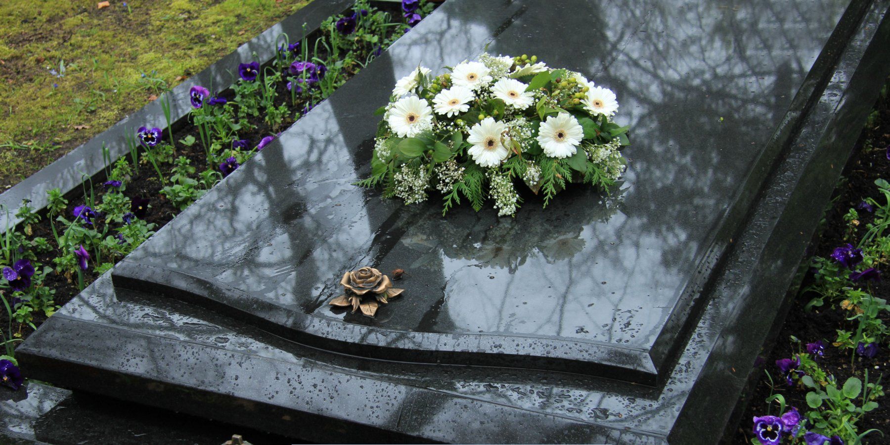 White floral arrangement resting on a polished gravestone in a cemetery, representing Funeral Home and Cremations in Leominster, MA