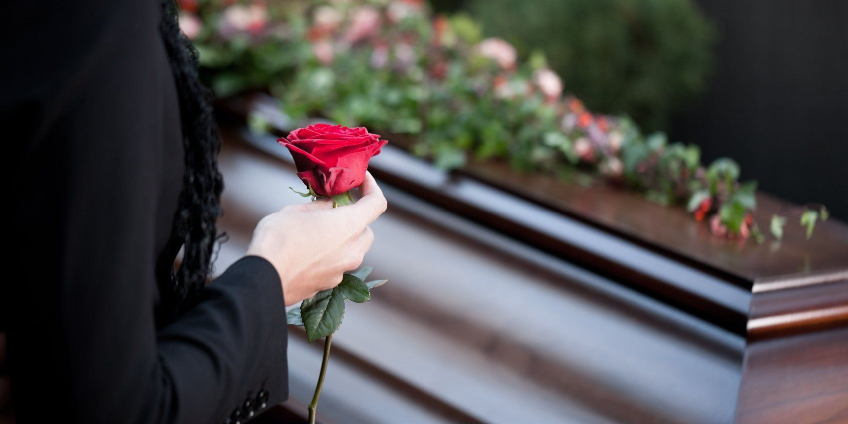 Mourner holding a red rose beside a casket at a memorial service for Funeral Home and Cremations in Worcester, MA.