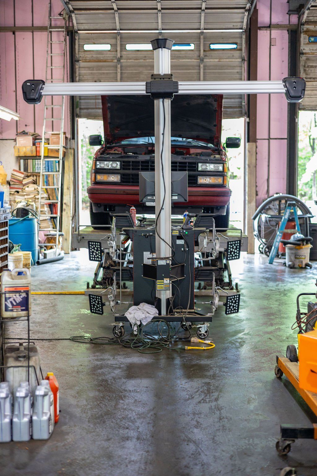 Car being aligned on a lift in a garage. Alignment machine with sensors, open hood, red truck.