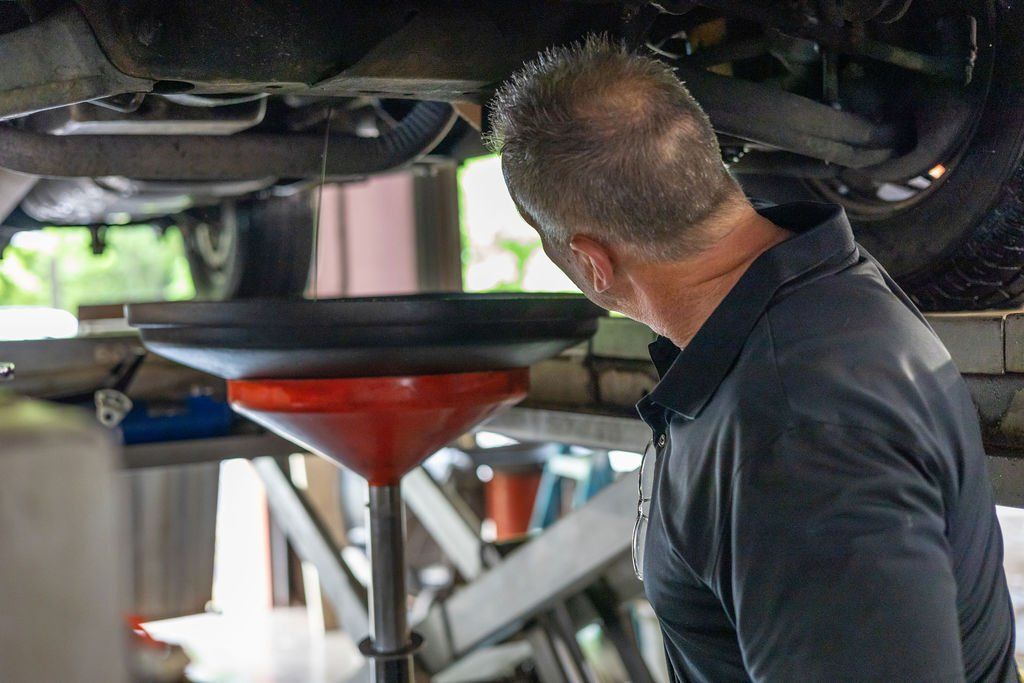 Mechanic inspecting a car's undercarriage as oil drains into a catch basin. The car is on a lift.