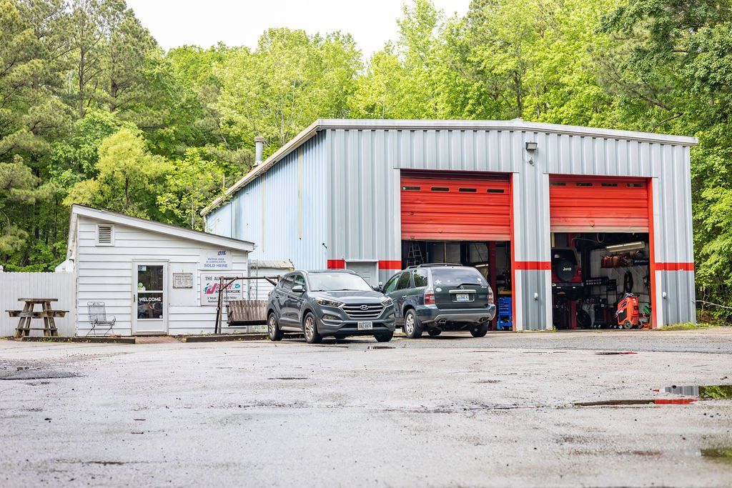 Auto repair shop with red garage doors, two cars parked outside, and a small office.