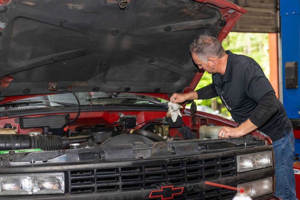 Mechanic cleaning engine in red truck, open hood, in a garage setting.