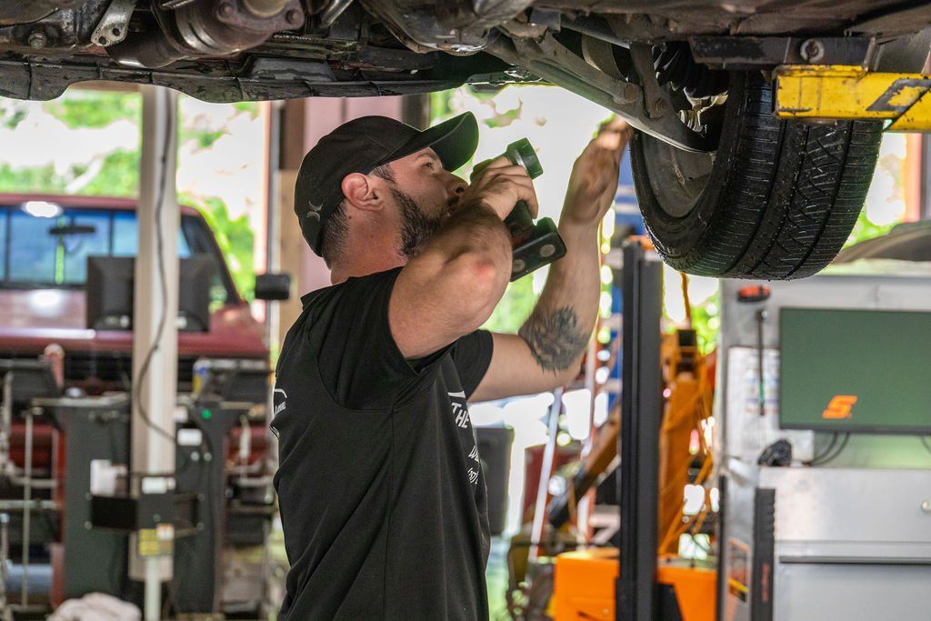 Mechanic working under a car on a lift, using a drill. In a shop setting.