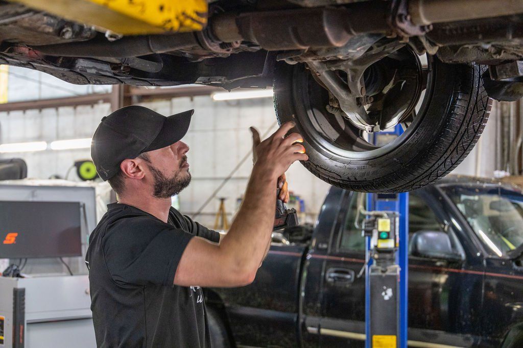 Mechanic examining car tire underneath a vehicle on a lift in a garage.