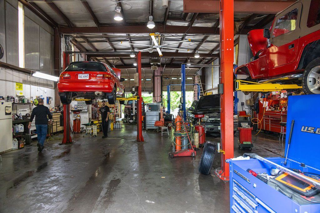 Inside a car repair shop with vehicles on lifts; workers in action. Red and blue cars.