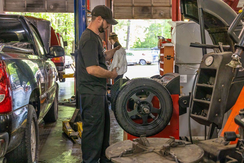 Mechanic balancing a tire in a garage, with another person in the background.