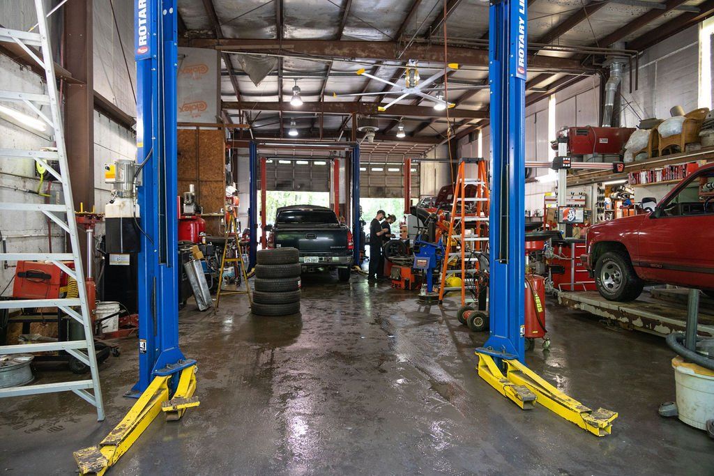 Auto repair shop with two-post lifts, car, tires, tools, and a wet floor.