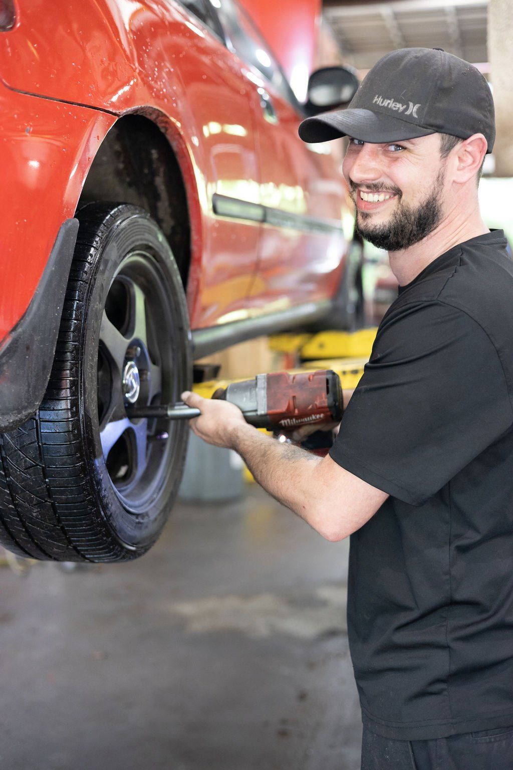 Mechanic removing a tire from a red car using a power tool in a garage.