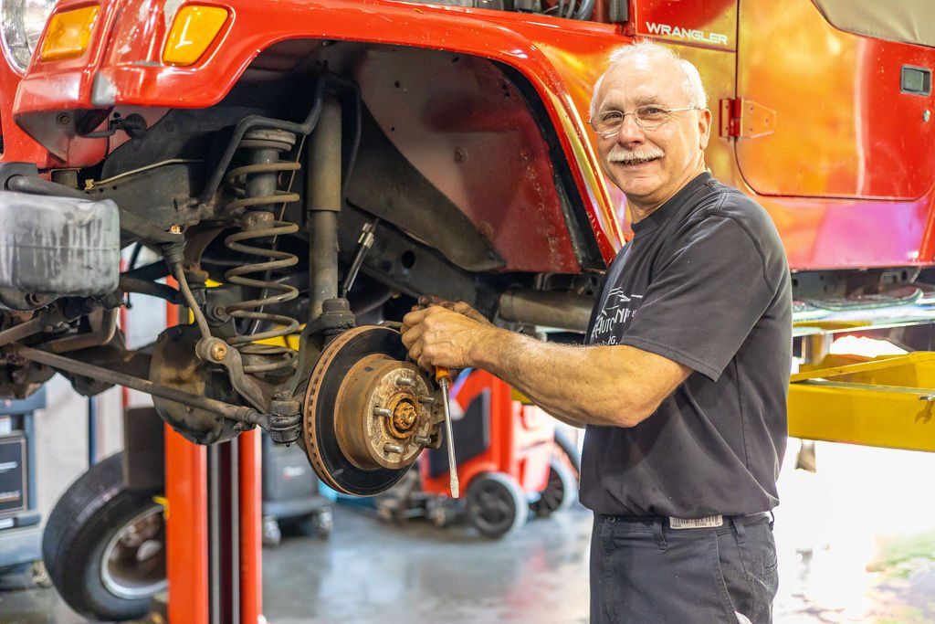 Mechanic working on a red Jeep, smiling. Holding a wrench, garage setting.