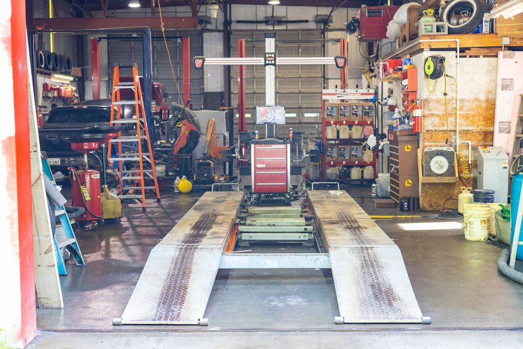 Car alignment machine in auto repair shop; mechanic working near ladder.