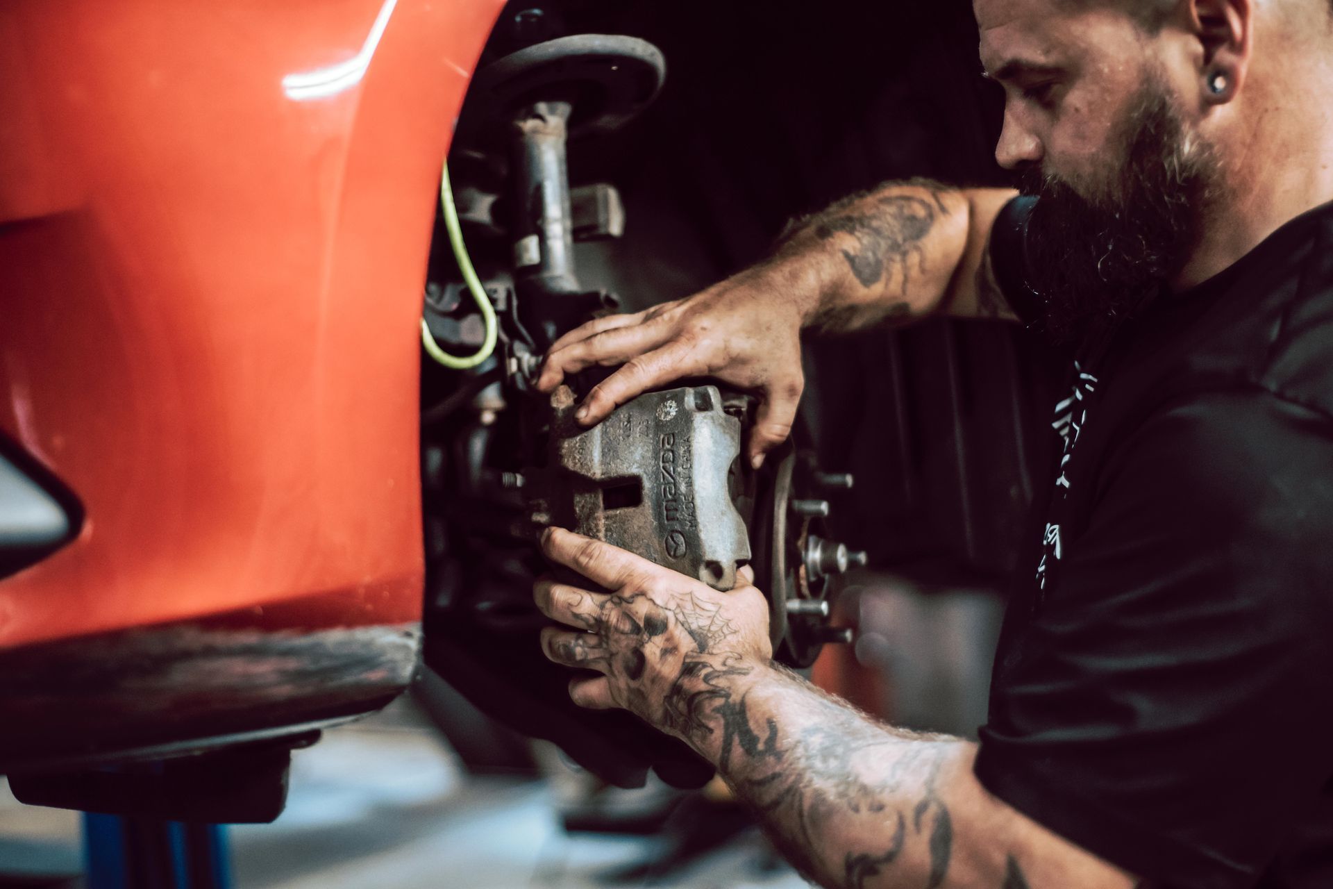 Mechanic working on a car brake. Red car, hands on brake caliper. Workshop setting.