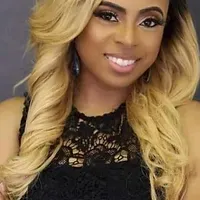 A woman with long blonde hair is wearing a black lace top and smiling.